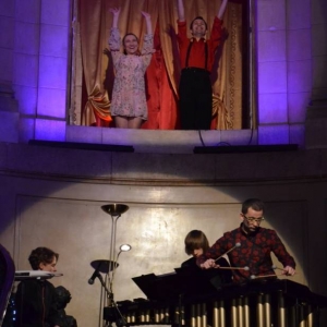 Zdjęcie przedstawia występujących artystów w witrynie okiennej oraz u szczytu schodów  wewnątrz Pałacu Kawalera,  podczas koncertu pt. Percussio