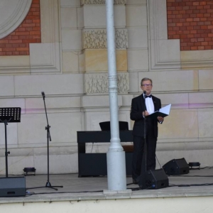 Zdjęcie przedstawia artystę na scenie amfiteatru w świerklanieckim parku podczas koncertu pt. O sole mio-kanikuła z pieśnią neapolitańską