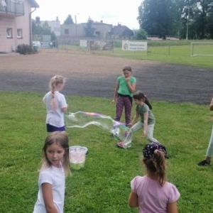 Zdjęcie przedstawia uczestników półkolonii podczas wspólnej zabawy na boisku sportowym