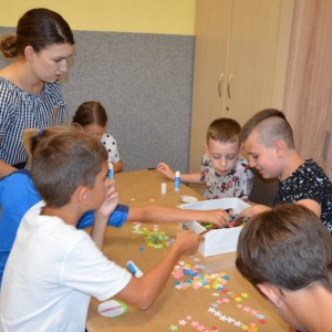 Zdjęcie przedstawia uczestników półkolonii podczas wykonywania pracy plastycznej oraz wychowawcę półkolonii