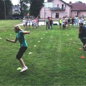 Zdjęcie przedstawia uczestników półkolonii podczas wspólnej zabawy na boisku sportowym