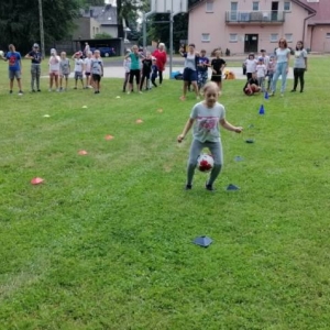 Zdjęcie przedstawia uczestników półkolonii podczas wspólnej zabawy na boisku sportowym
