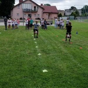 Zdjęcie przedstawia uczestników półkolonii podczas wspólnej zabawy na boisku sportowym