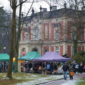 Zdjęcie przedstawia świąteczny jarmark, który zachęca do zakupu prezentów i ciepłych napojów