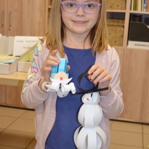 Zdjęcie przedstawia uczestniczkę Rodzinnych Warsztatów Świątecznych z wykonanymi choinkowymi ozdobami z papieru 