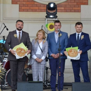 Zdjęcie przedstawia uroczyste przekazanie chlebów przez Starostów Dożynkowych Włodarzom Gminy