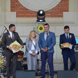 Zdjęcie przedstawia uroczyste przekazanie chlebów przez Starostów Dożynkowych Włodarzom Gminy