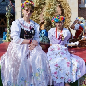 Dziewczyny w strojach ludowych a w tle korona dożynkowa