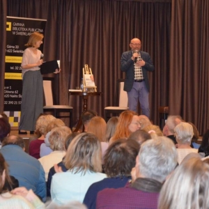 Artur Barciś i prowadząca spotkanie Anna Kempa-Gąsior na scenie podczas spotkania autorskiego. Przed sceną publiczność.