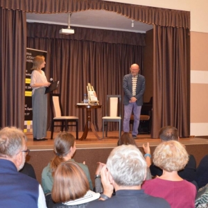 Artur Barciś i prowadząca spotkanie Anna Kempa-Gąsior na scenie podczas spotkania autorskiego. Przed sceną publiczność.