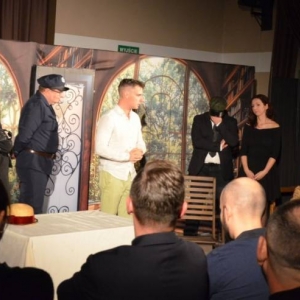Aktorzy na scenie podczas spektaklu. Przed sceną publiczność.