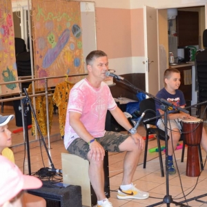 Zdjęcie przedstawia prowadzącego oraz uczestników półkolonii podczas warsztatów muzycznych