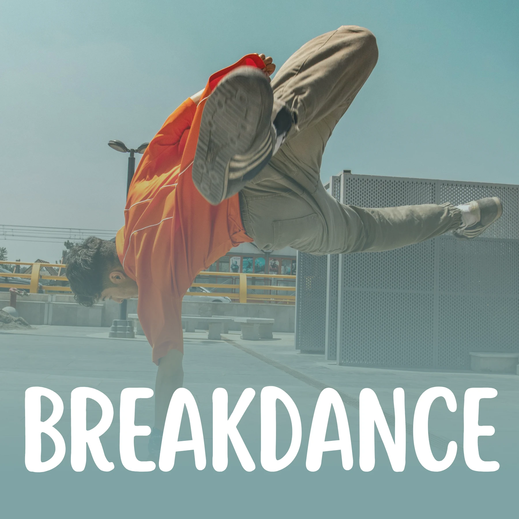 Młody mężczyzna w pomarańczowej koszulce wykonuje skomplikowaną figurę breakdance, balansując na jednej ręce na betonowym placu. Na dole zdjęcia umieszczono duży, biały napis „BREAKDANCE”.